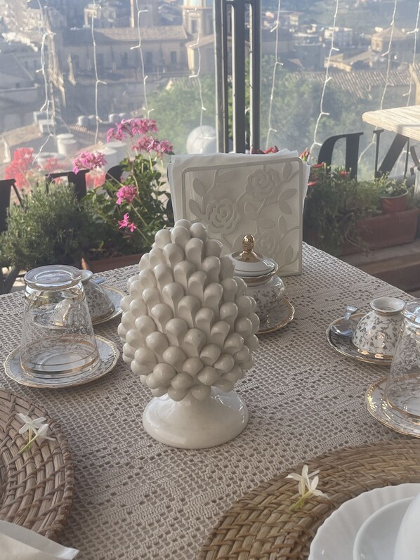 Una mesa dispuesta con vajilla blanca, incluyendo un florero, tazas de té y un azucarero, sobre un mantel con textura.