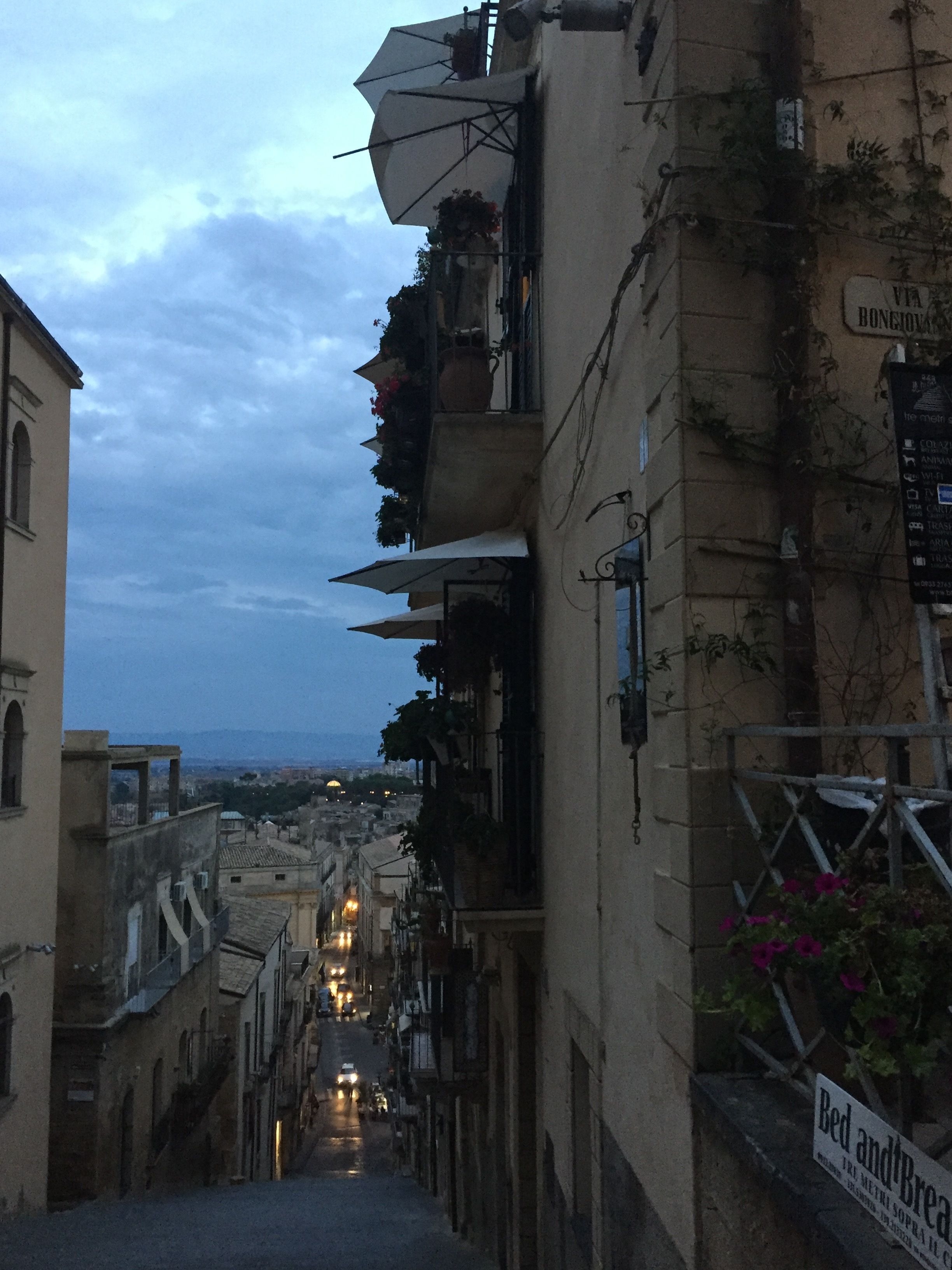 Une rue étroite, bordée de bâtiments des deux côtés, dont certains sont dotés de balcons et d’espaces de sièges en plein air.