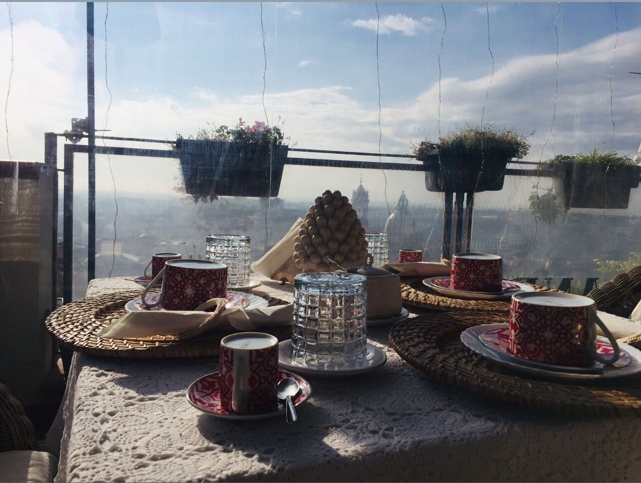 Una mesa dispuesta con tazas rojas estampadas, un recipiente de vidrio y una cesta tejida.