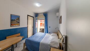Un dormitorio con cama, escritorio y silla. Se ve una ventana con cortinas, un cuadro en la pared y una puerta que da a otra habitación.