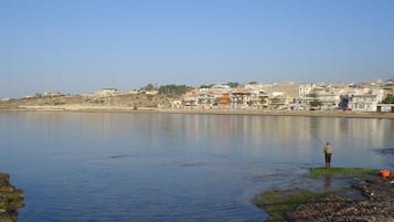 A coastal town with buildings along the shore and a person fishing in the water.