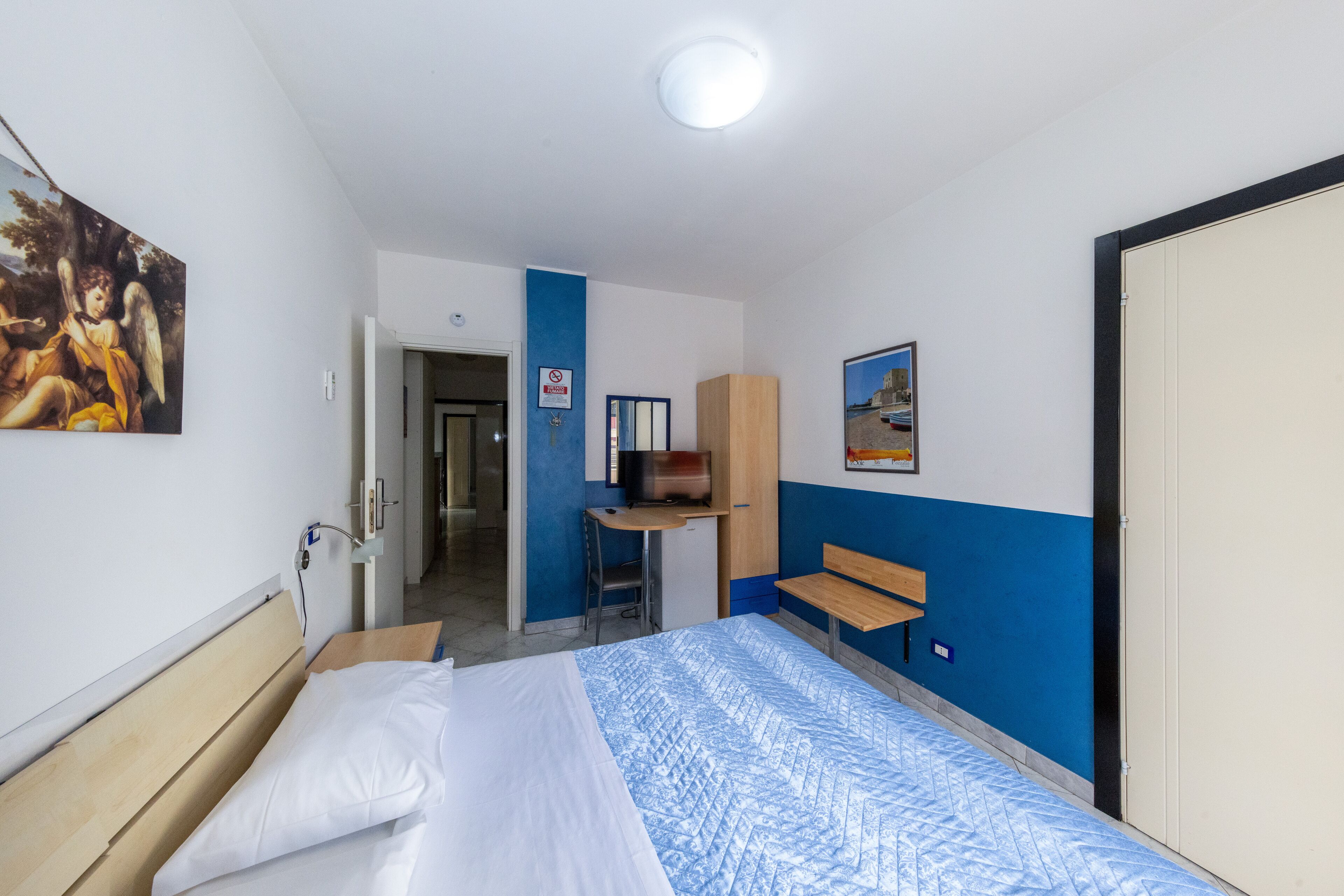 Une chambre d’hôtel avec un lit, un bureau, une chaise, une télévision et un tableau au mur.