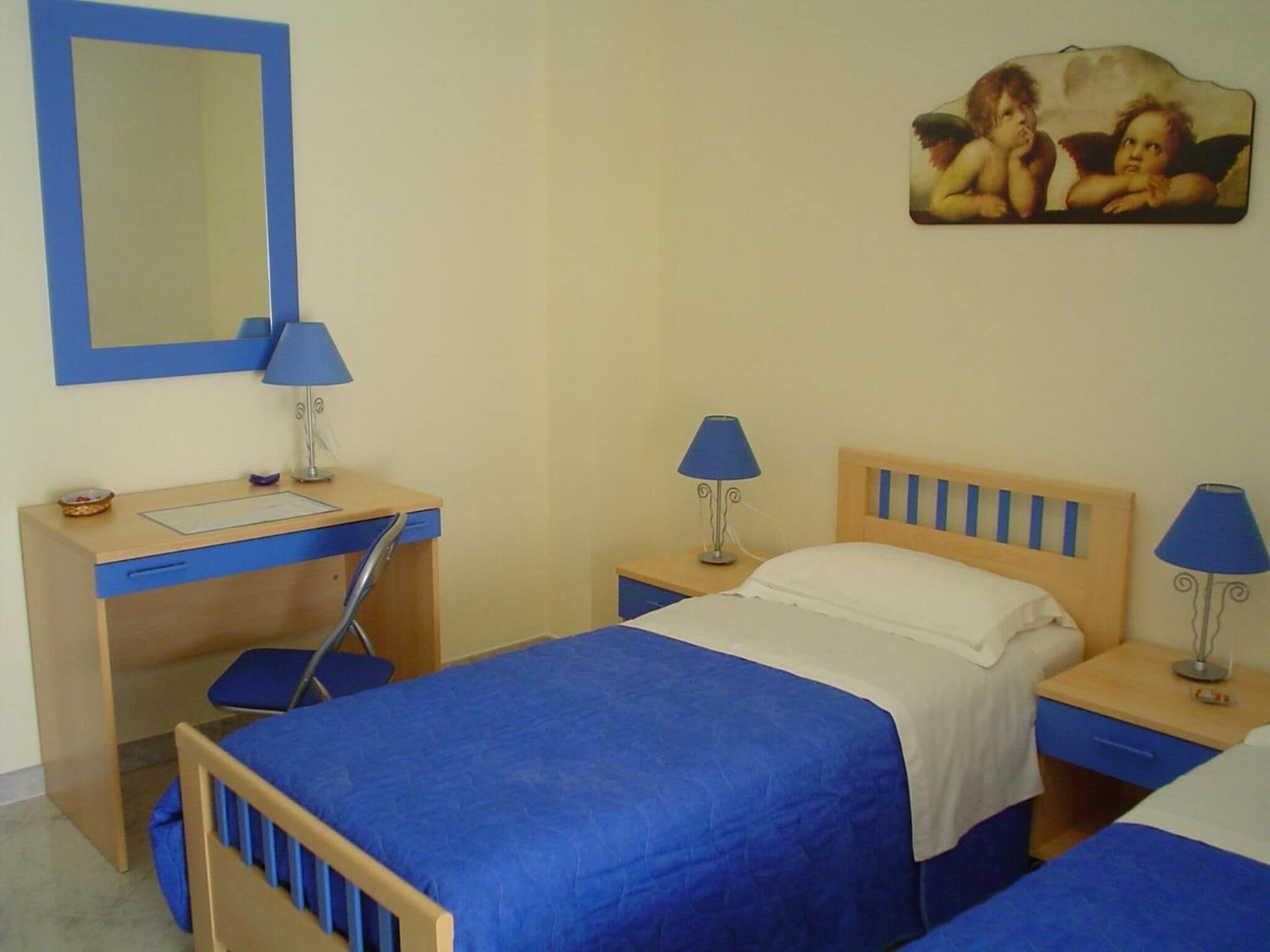 A bedroom with a bed, a desk, a chair, and a nightstand.