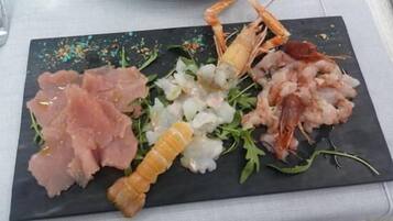 Una pizarra de pizarra negra con diversos mariscos, como camarones, vieiras y posiblemente algún tipo de carne curada, sobre un mantel blanco.
