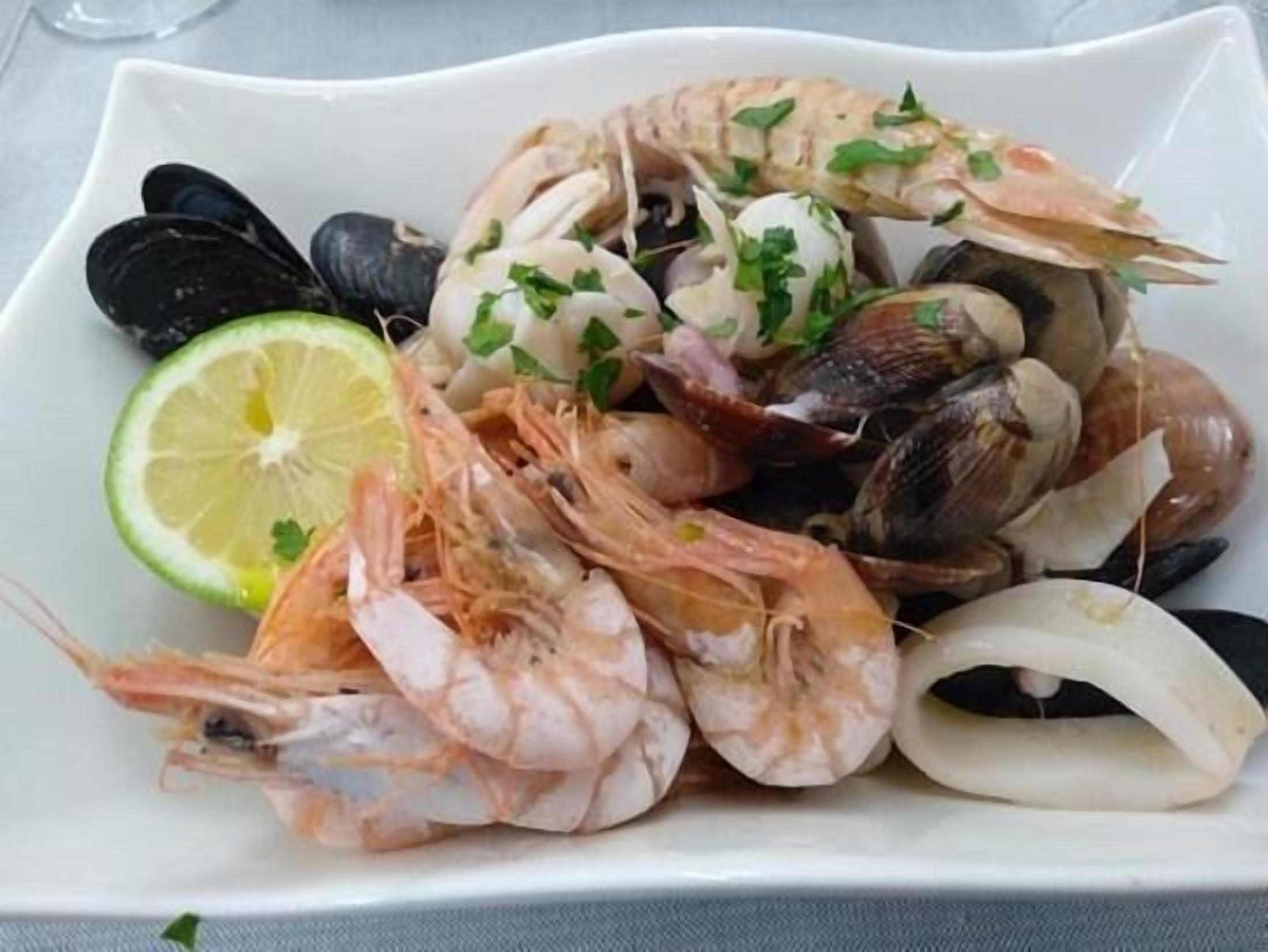 A plate of seafood including shrimp, mussels, clams, and squid, garnished with parsley and a slice of lime.