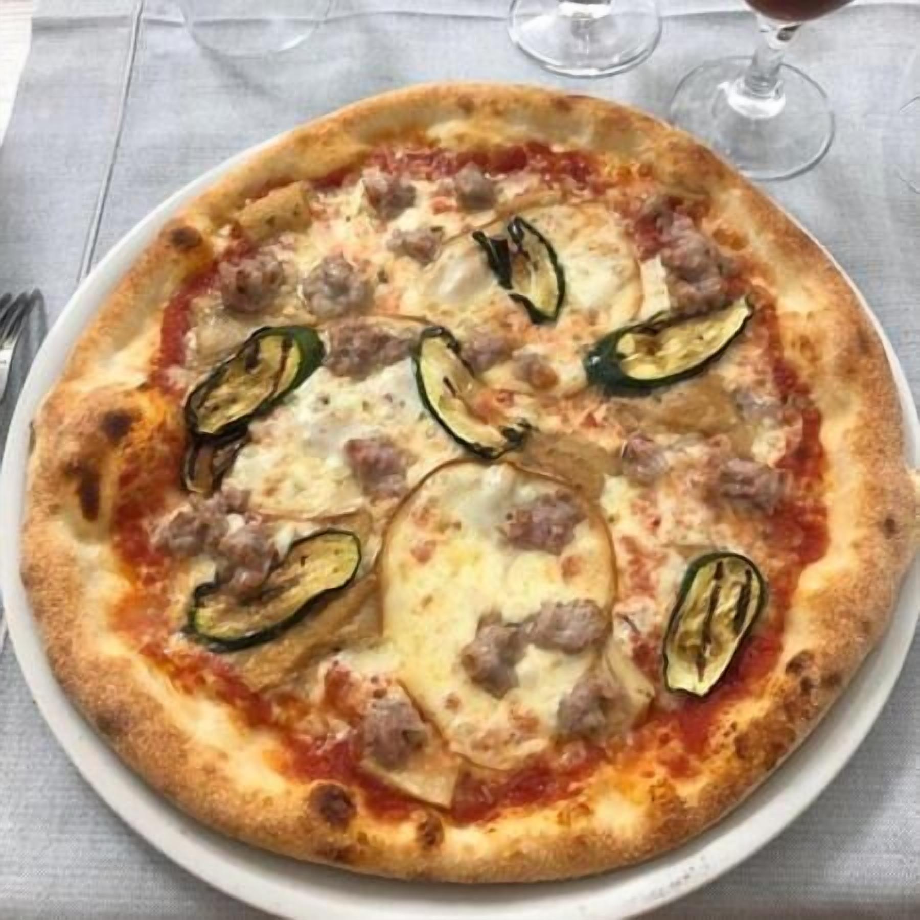 Pizza com salsicha, queijo e fatias de courgette numa travessa branca.