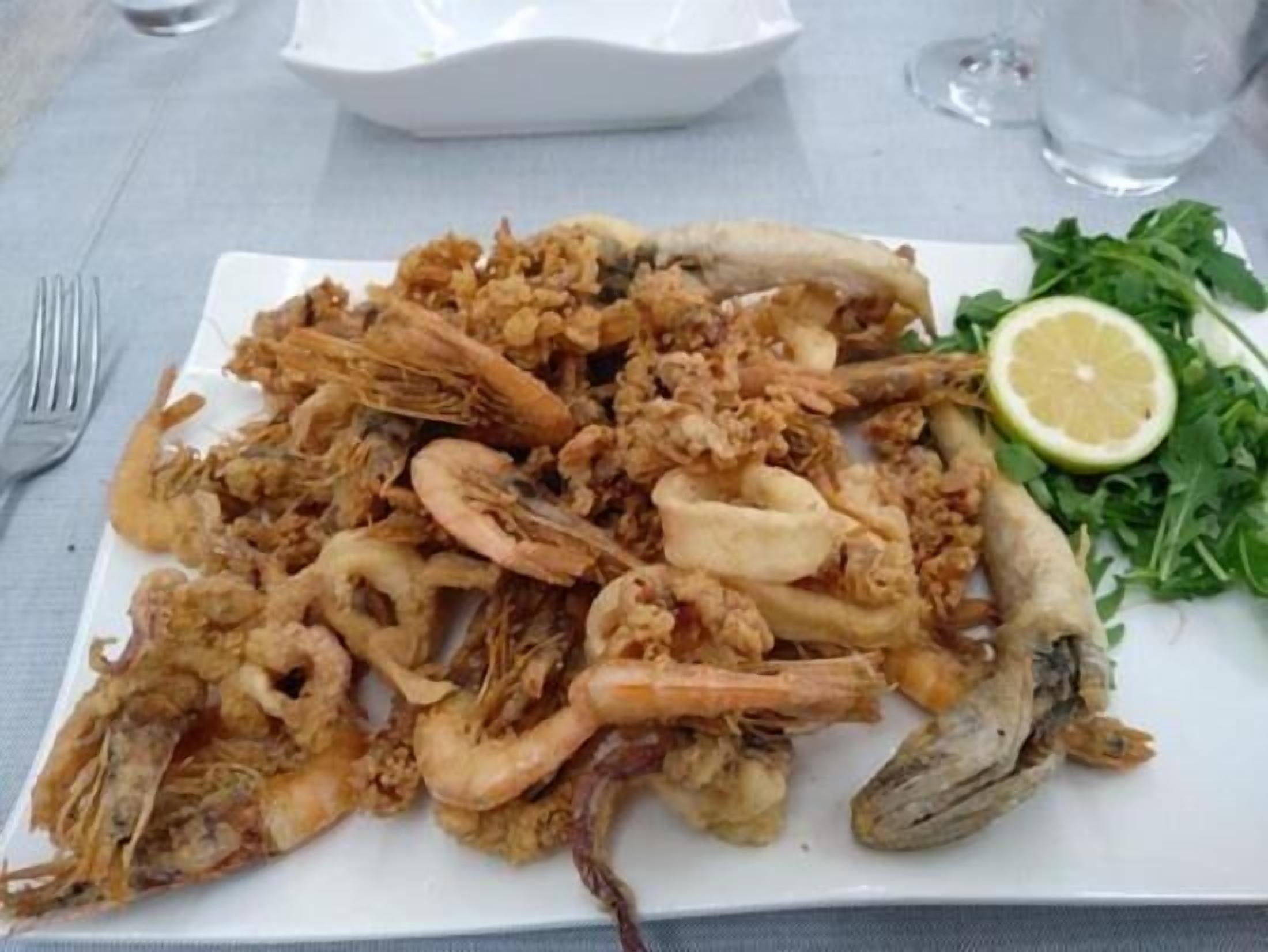Ein Teller gebratenem Meeresfrüchte, darunter Garnelen und Calamari, serviert mit einem Zitronenschnitz und etwas Grünzeug.