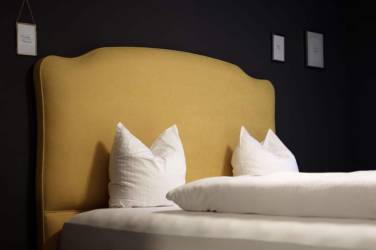 A bed with a mustard-colored headboard and white pillows.