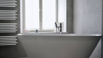 Un baño moderno con una bañera independiente, una ventana con persianas y un perchero para toallas.