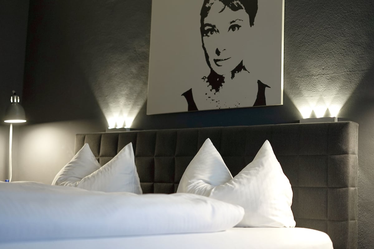 A bedroom with a tufted headboard, white bedding, and a framed artwork above the bed.