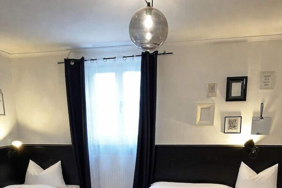 A hotel room with two beds, a wooden floor, a table, and a ceiling light.