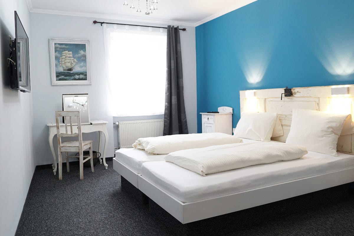 A hotel room with a bed, a desk, a chair, a painting, and a window.