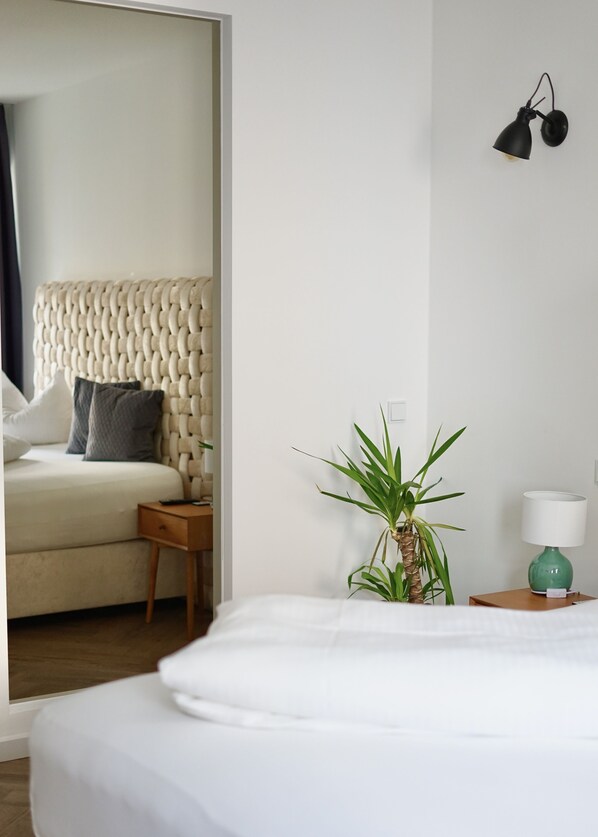 A hotel room with a bed, a nightstand, a lamp, a wall-mounted lamp, and a potted plant. - Hotel Mühldorf (Muhldorf am Inn)