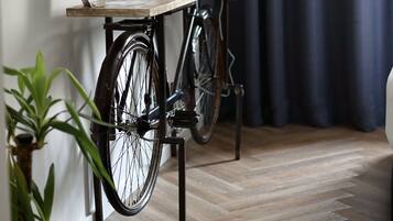 A room with a bicycle mounted on a wooden stand, a flat-screen TV on the wall, and a potted plant.
