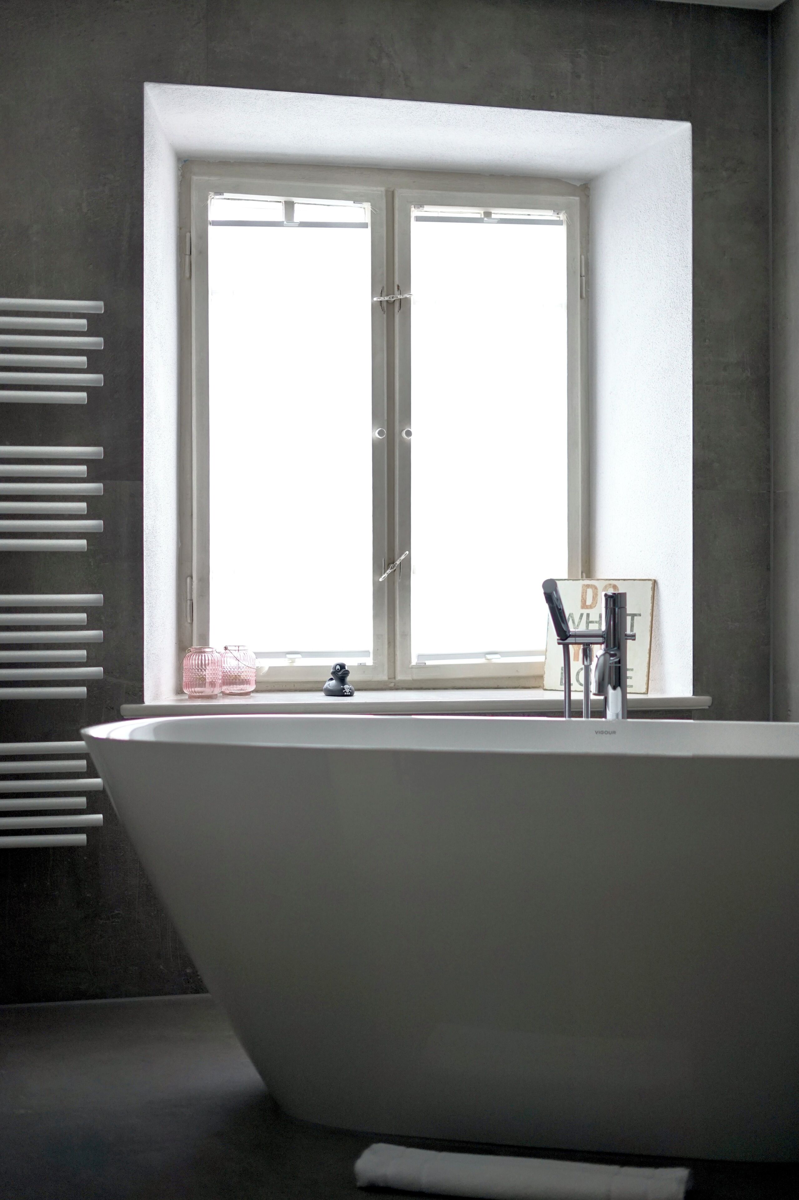 A modern bathroom with a freestanding bathtub, a window with blinds, and a towel rack.
