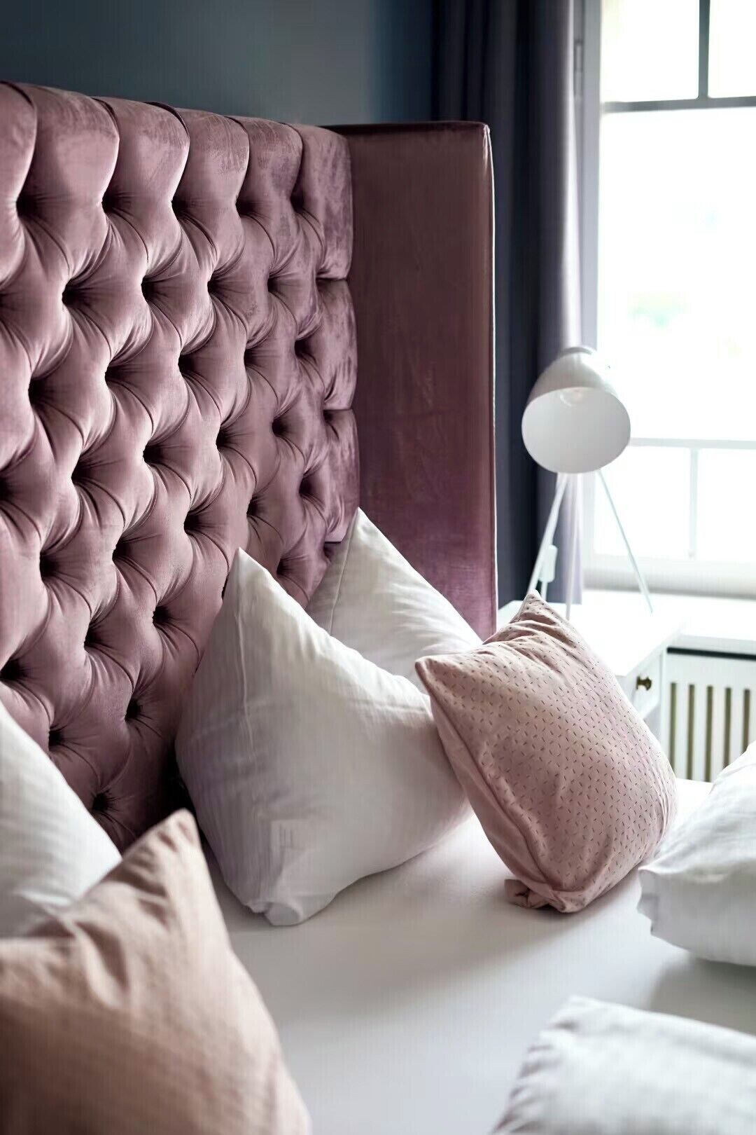A bedroom with a tufted headboard, white and pink pillows, and a bedside lamp.