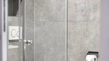 Un baño moderno con inodoro, cabina de ducha de vidrio y una toalla en un perchero.