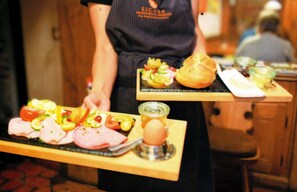 A person serving food on a wooden board with various items including bread, vegetables, and a boiled egg. - Hotel Mühldorf (Muhldorf am Inn)