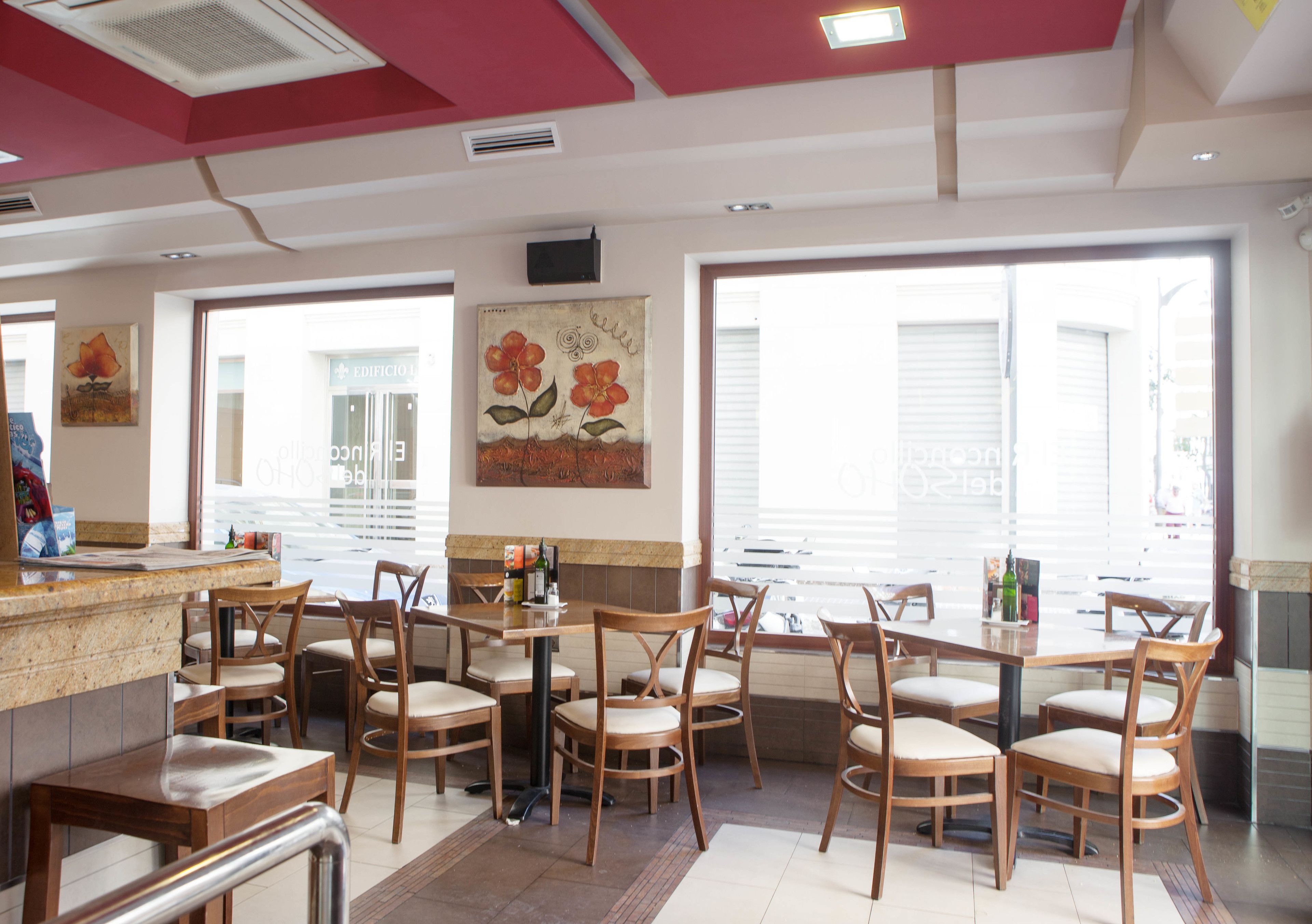 L’intérieur d’un restaurant avec des tables et des chaises en bois, un comptoir et de grandes fenêtres équipées de stores.