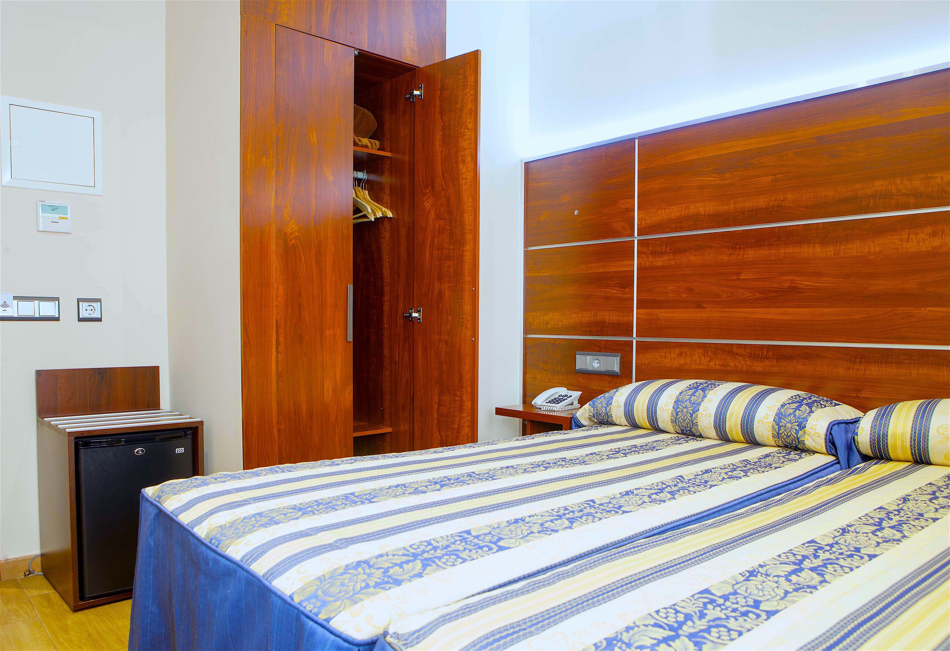 Ein Hotelzimmer mit Bett, Schrank, Schreibtisch und kleinem Kühlschrank.