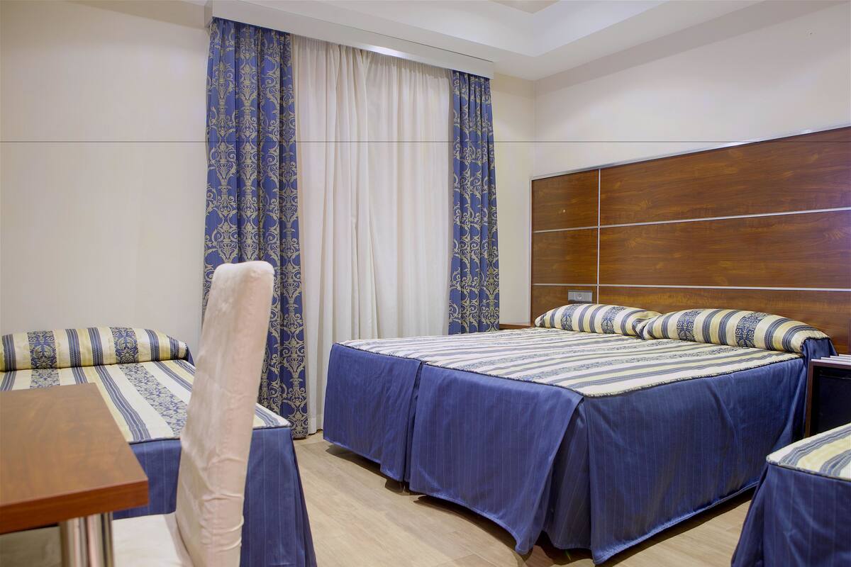 A hotel room with two beds, a wooden headboard, a small table, and a chair.