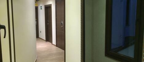 A corridor with a wooden floor, a glass door with a metal frame, and a door with a dark wooden finish.