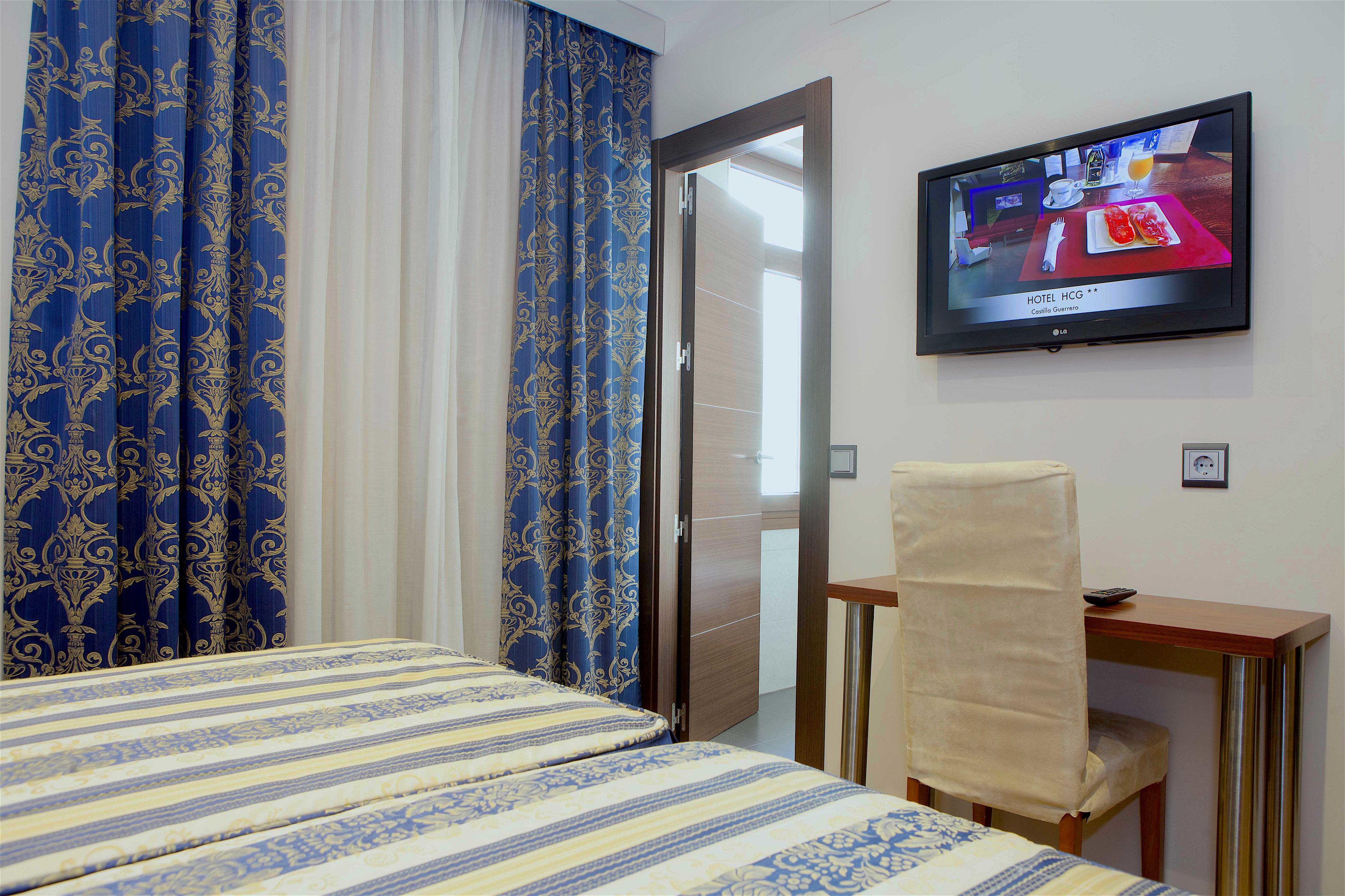 Una habitación de hotel con una cama, un escritorio, una silla, un televisor y cortinas.