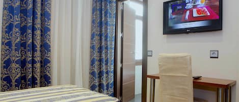Una habitación de hotel con una cama, un escritorio, una silla, un televisor y cortinas.