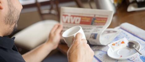 Una persona llegint un diari amb una tassa i una cullera damunt d'una taula.