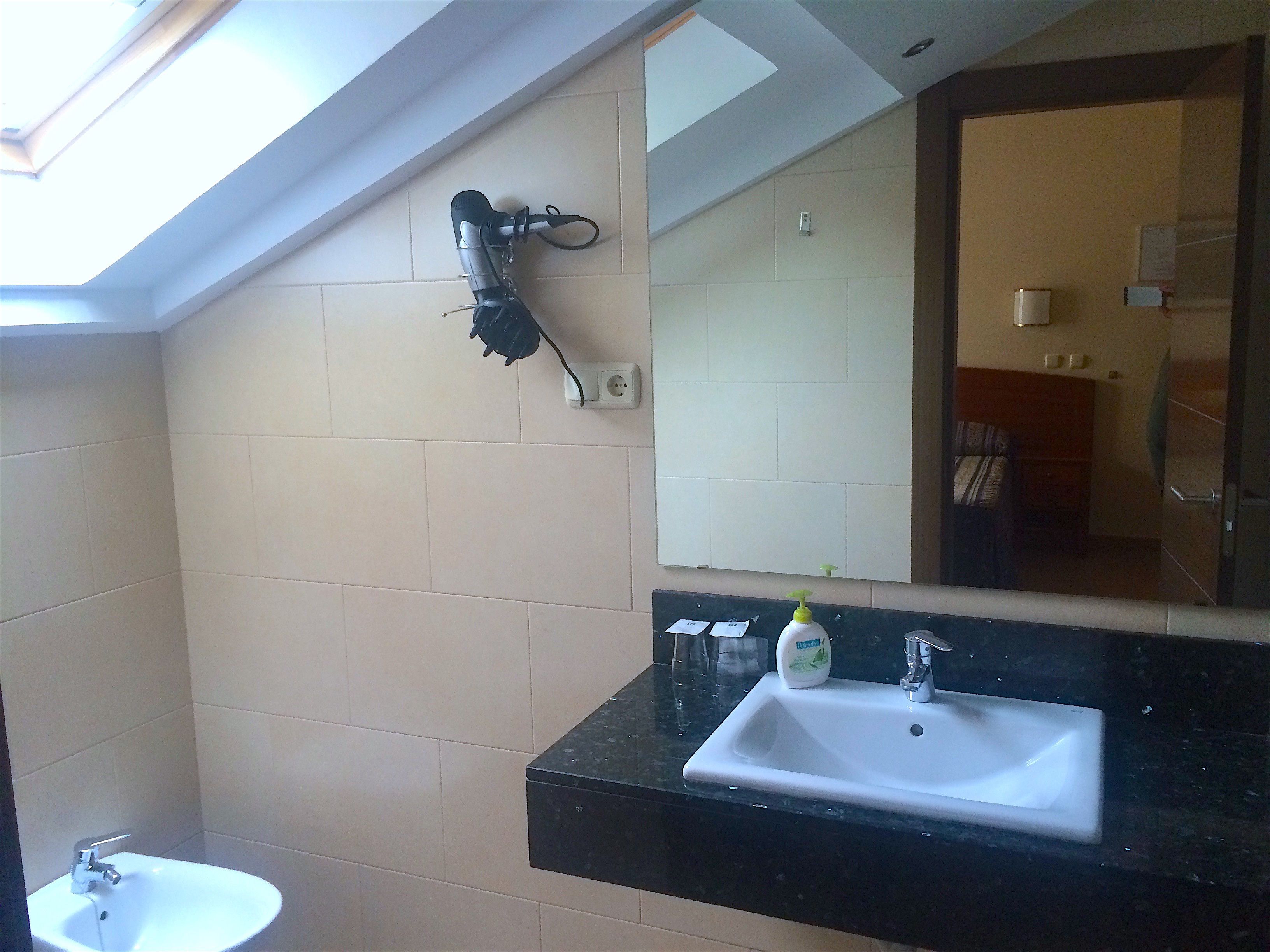 A bathroom with a black countertop sink, a mirror, and a hairdryer mounted on the wall.