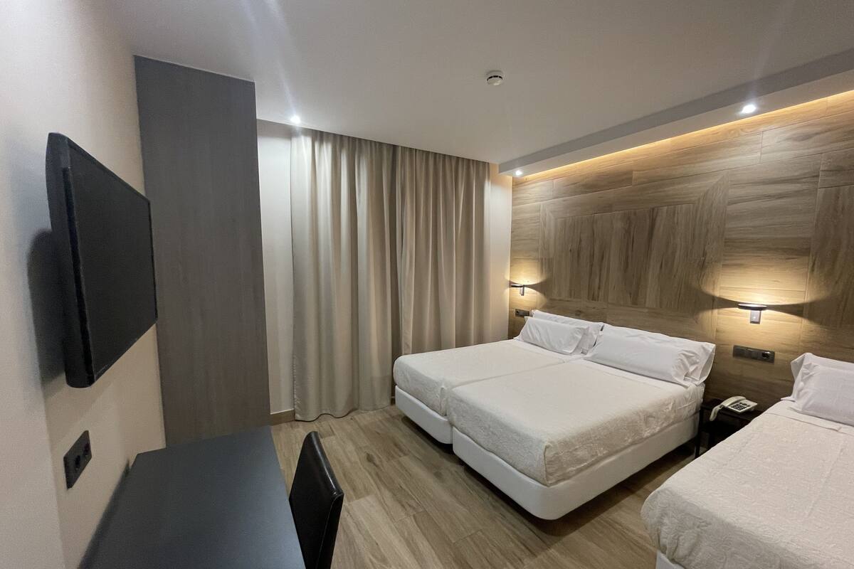 A modern hotel room with a large bed, a desk, and a TV mounted on the wall.