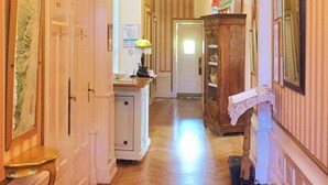 A hallway with a wooden herringbone floor, a chandelier, and a wooden cabinet with a painting on top. - Hotel Le Manoir (Barr)