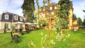 A large, two-story building with a garden patio area featuring outdoor seating and umbrellas. - Hotel Le Manoir (Barr)