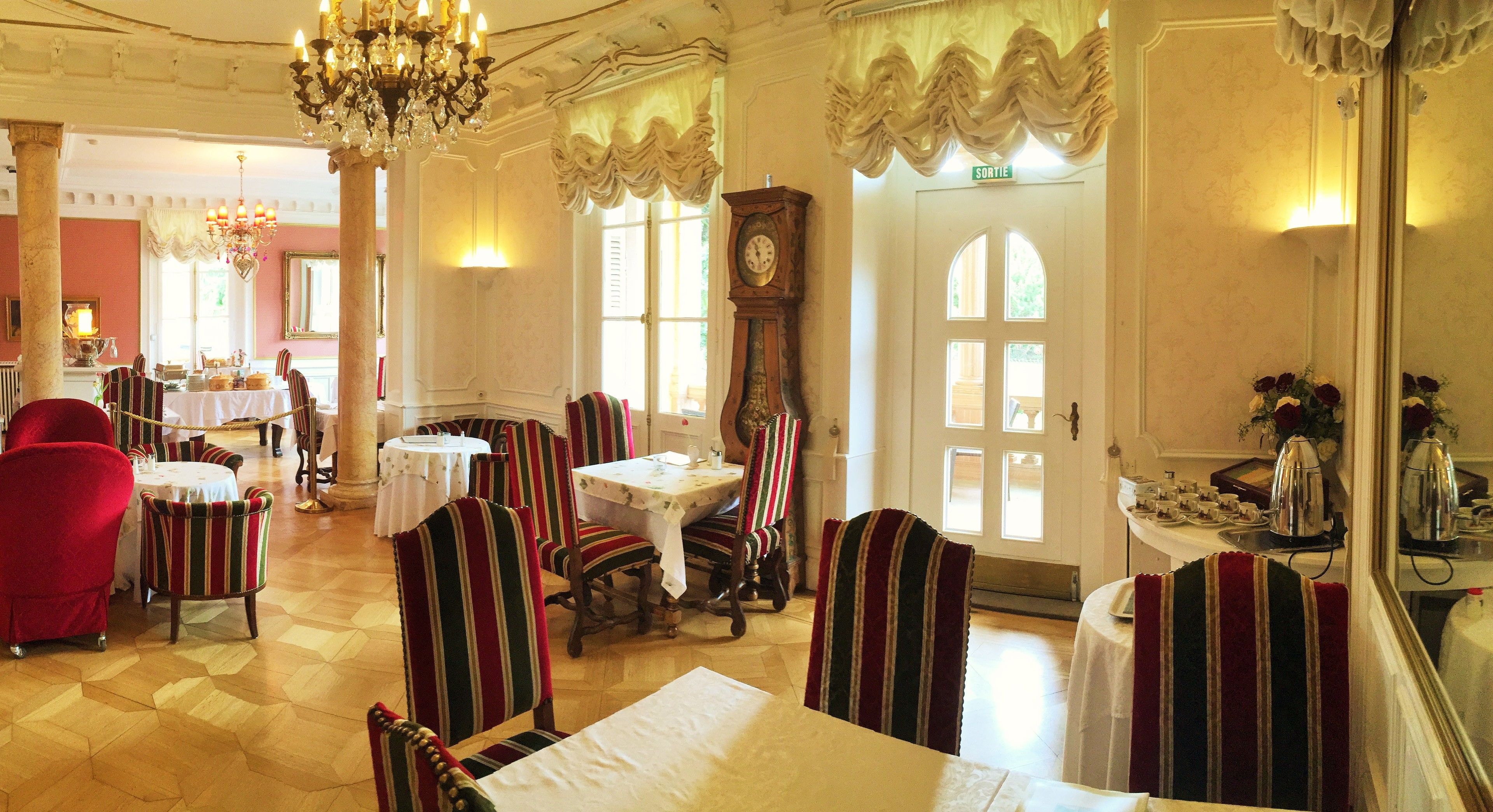 A dining area with striped chairs and tables, a chandelier, and a clock on the wall.