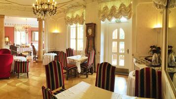 A dining area with striped chairs and tables, a chandelier, and a clock on the wall.