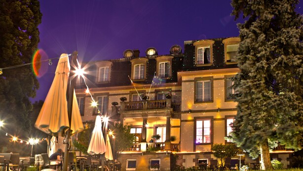 A multi-story building with balconies, outdoor seating, and string lights. - Hotel Le Manoir (Barr)