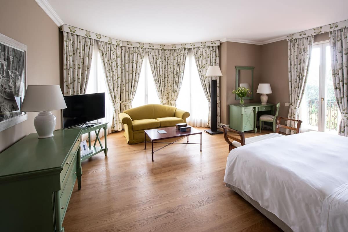 A hotel room with a bed, a sofa, a desk, a television, and a lamp.