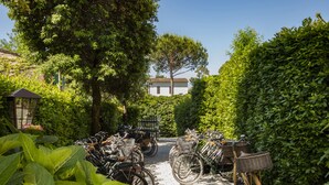 A gravel path lined with bicycles and baskets, surrounded by lush greenery and trees. - Hotel Franceschi (Forte dei Marmi)