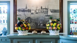 A framed historical painting of a harbor scene with two fruit baskets in front. - Hotel Franceschi (Forte dei Marmi)