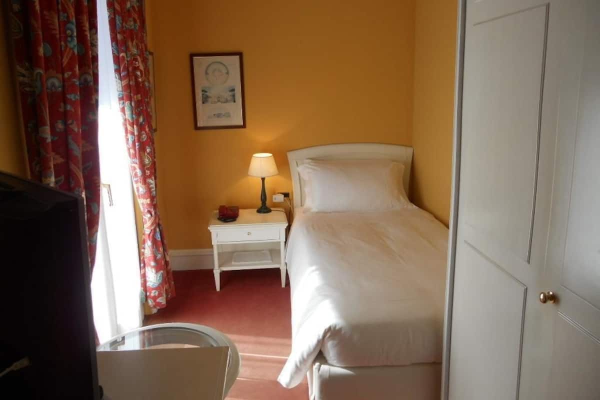 A hotel room with a bed, a nightstand with a lamp, a framed picture on the wall, and a door.