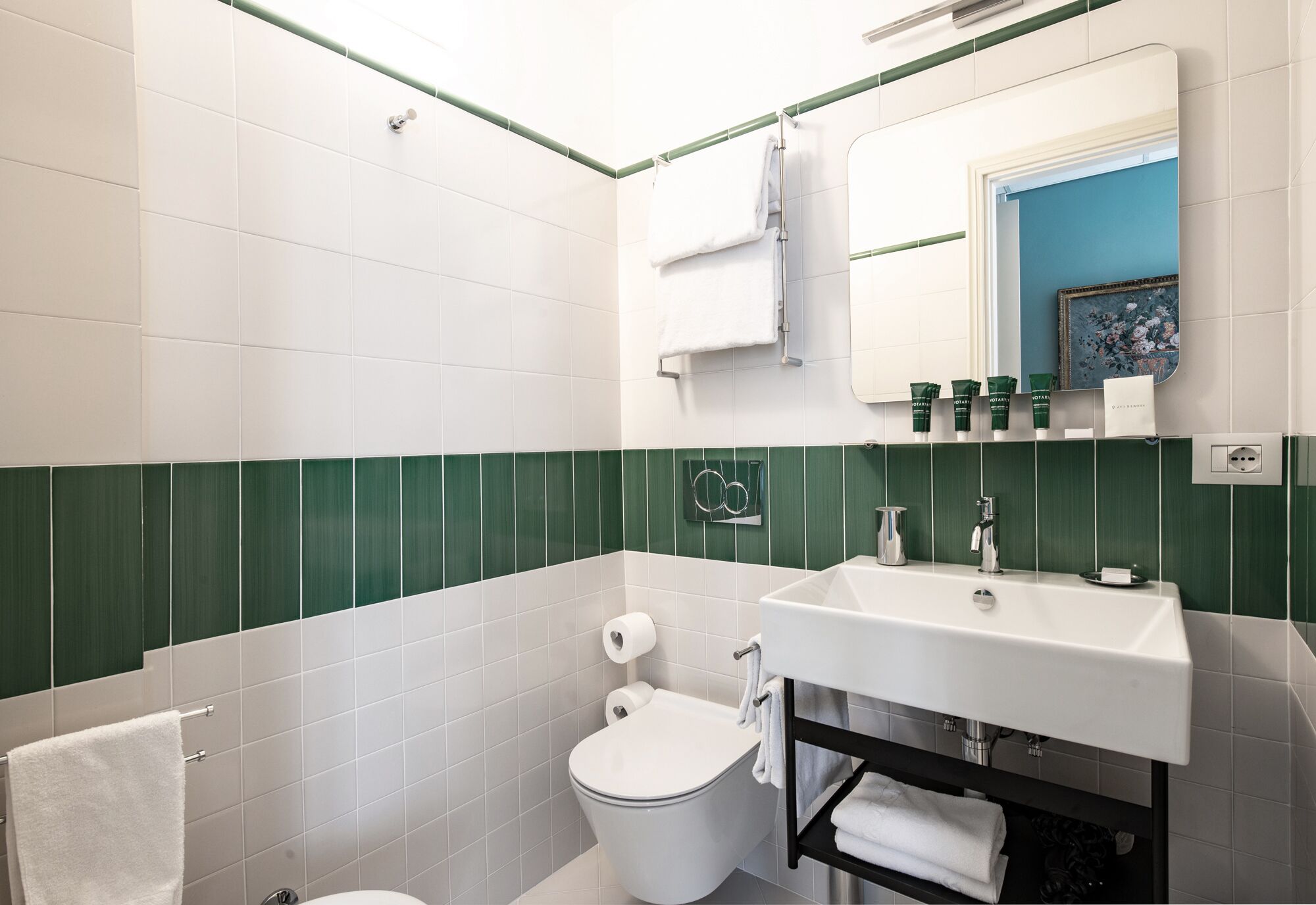 Un bagno con piastrelle bianche e verdi, un lavandino bianco, uno specchio e un water.