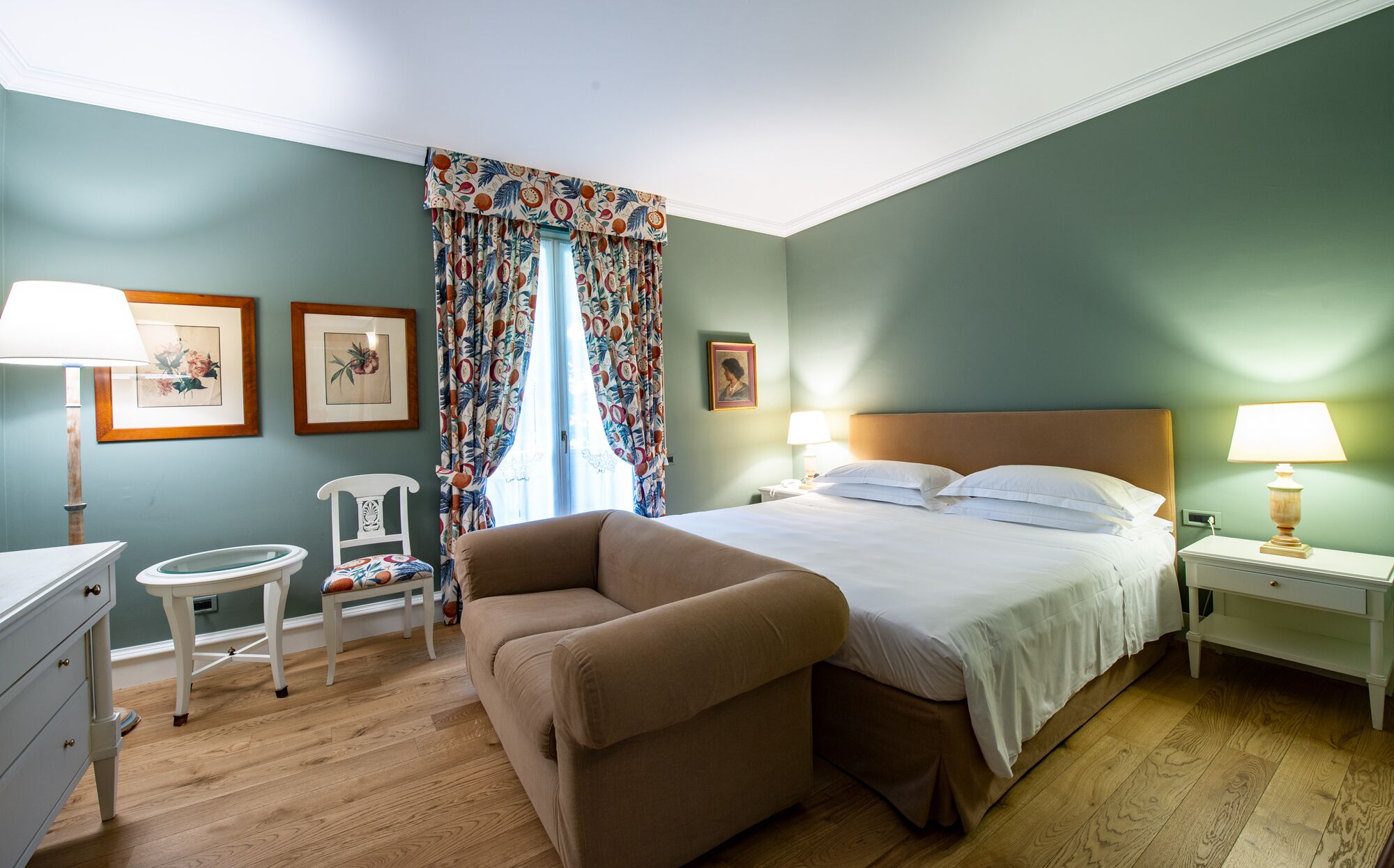 A bedroom with a bed, two bedside tables, a chair, a dresser, and a window with curtains.