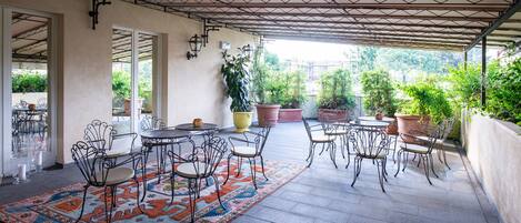 An outdoor patio with round tables and chairs, potted plants, and a patterned rug.
