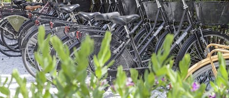 A row of bicycles parked in a covered area with greenery and flowers in the foreground.