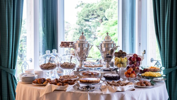 A buffet table with various food items and serving dishes, set against a backdrop of a window with curtains. - Hotel Franceschi (Forte dei Marmi)