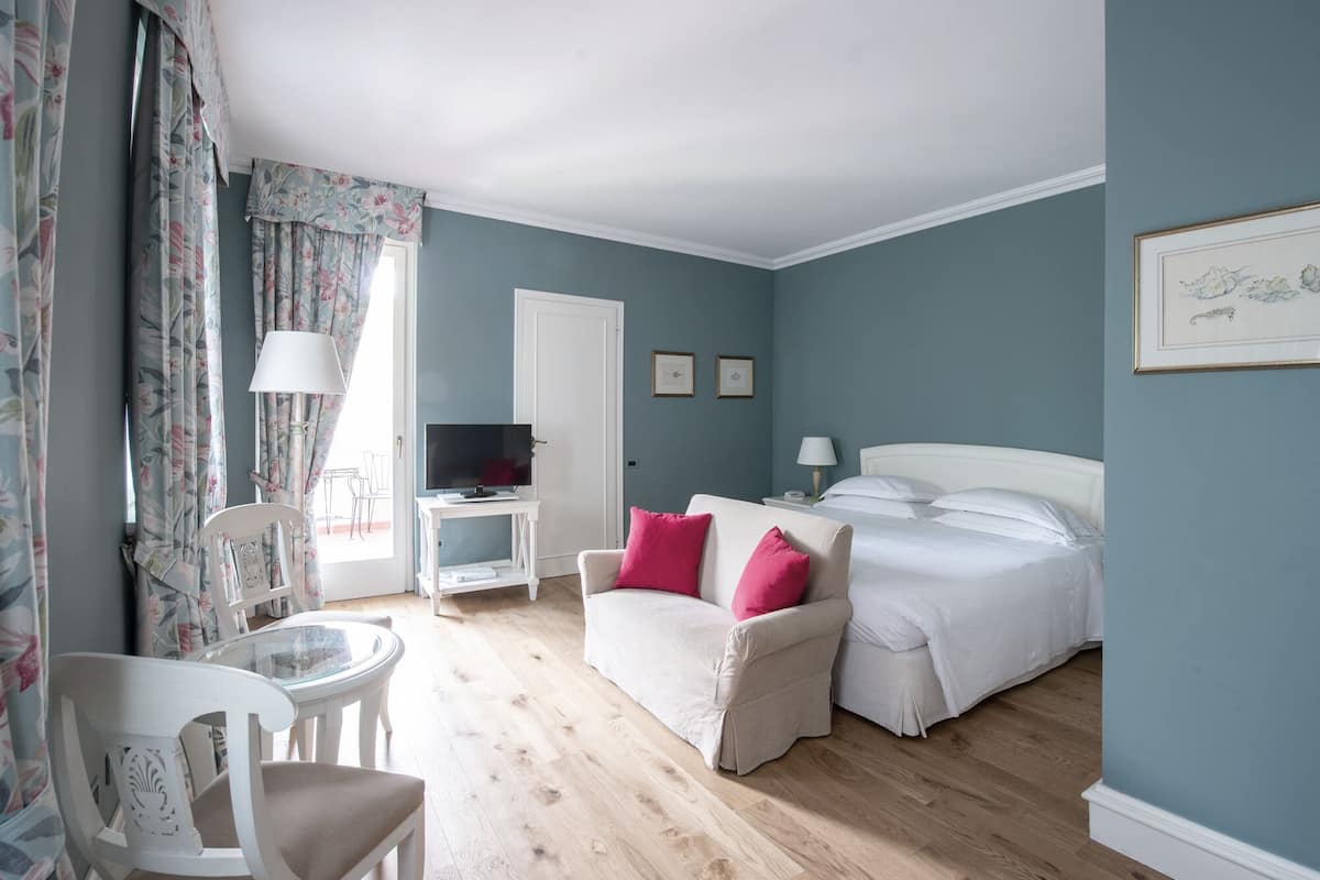 A bedroom with a bed, a chair, a small table, a TV, and a lamp.