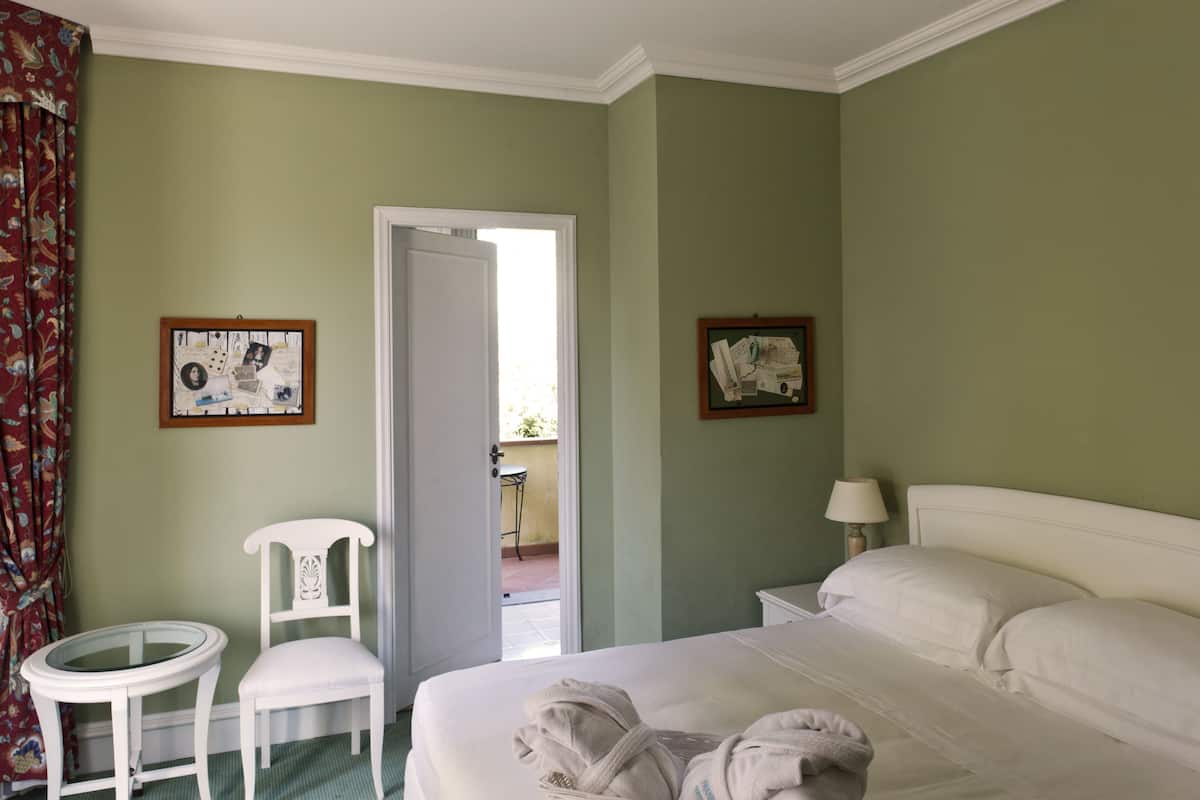 A hotel room with a bed, a chair, a small table, and two framed pictures on the walls.