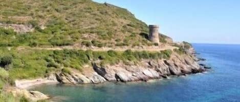 Un paisaje costero con una colina rocosa y una estructura similar a una torre.