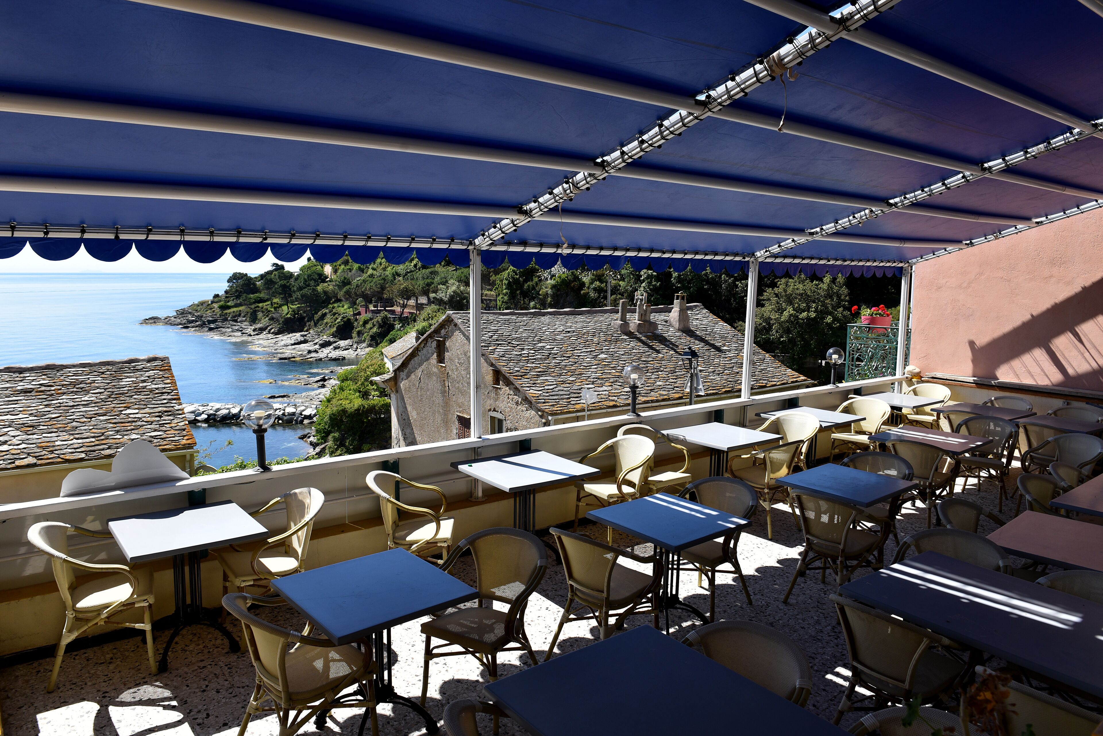 Une terrasse extérieure, dotée de tables et de chaises, qui offre une vue sur une zone côtière caractérisée par un terrain rocheux et une végétation luxuriante.