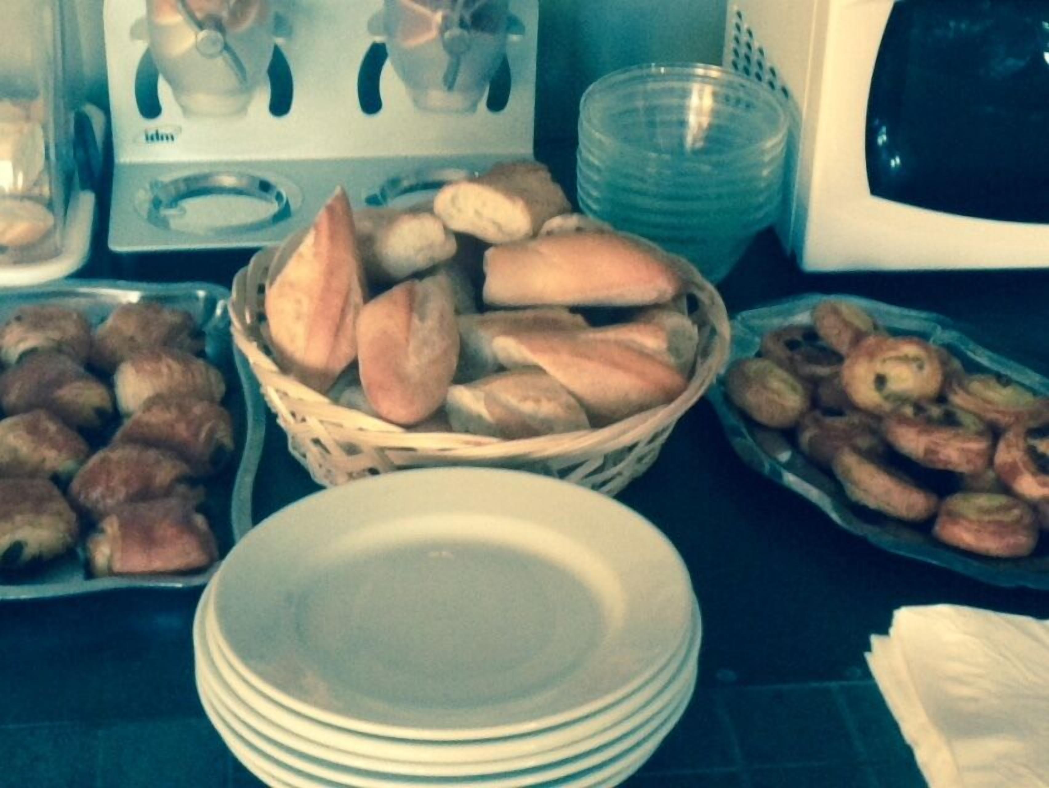 A kitchen counter with various food items, including bread and pastries, and a stack of white plates.